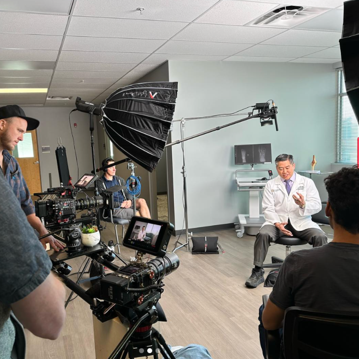 A man in a white coat is sitting in front of a camera