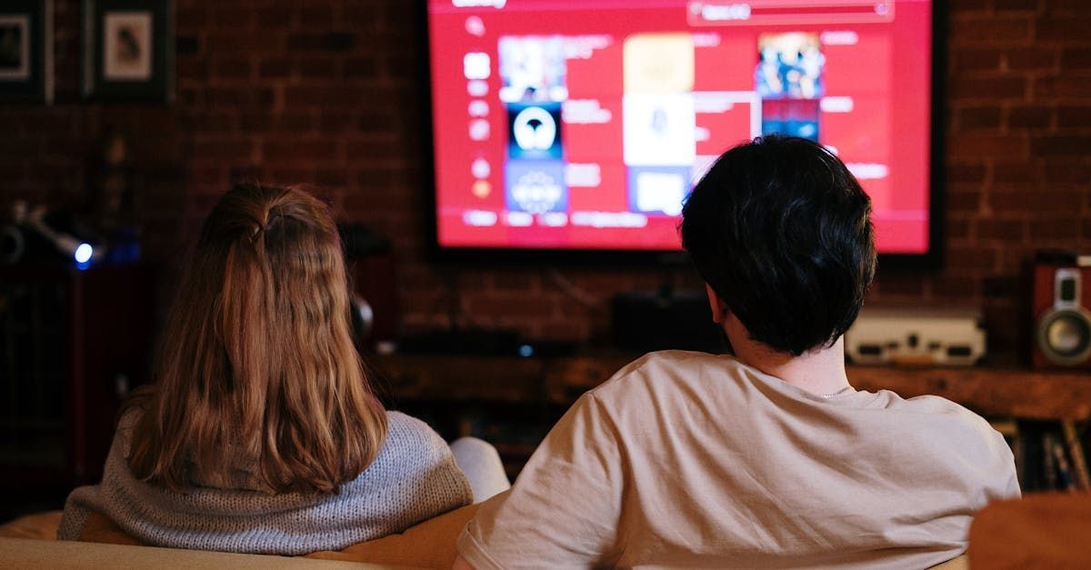 A man and a woman are sitting on a couch watching a television.