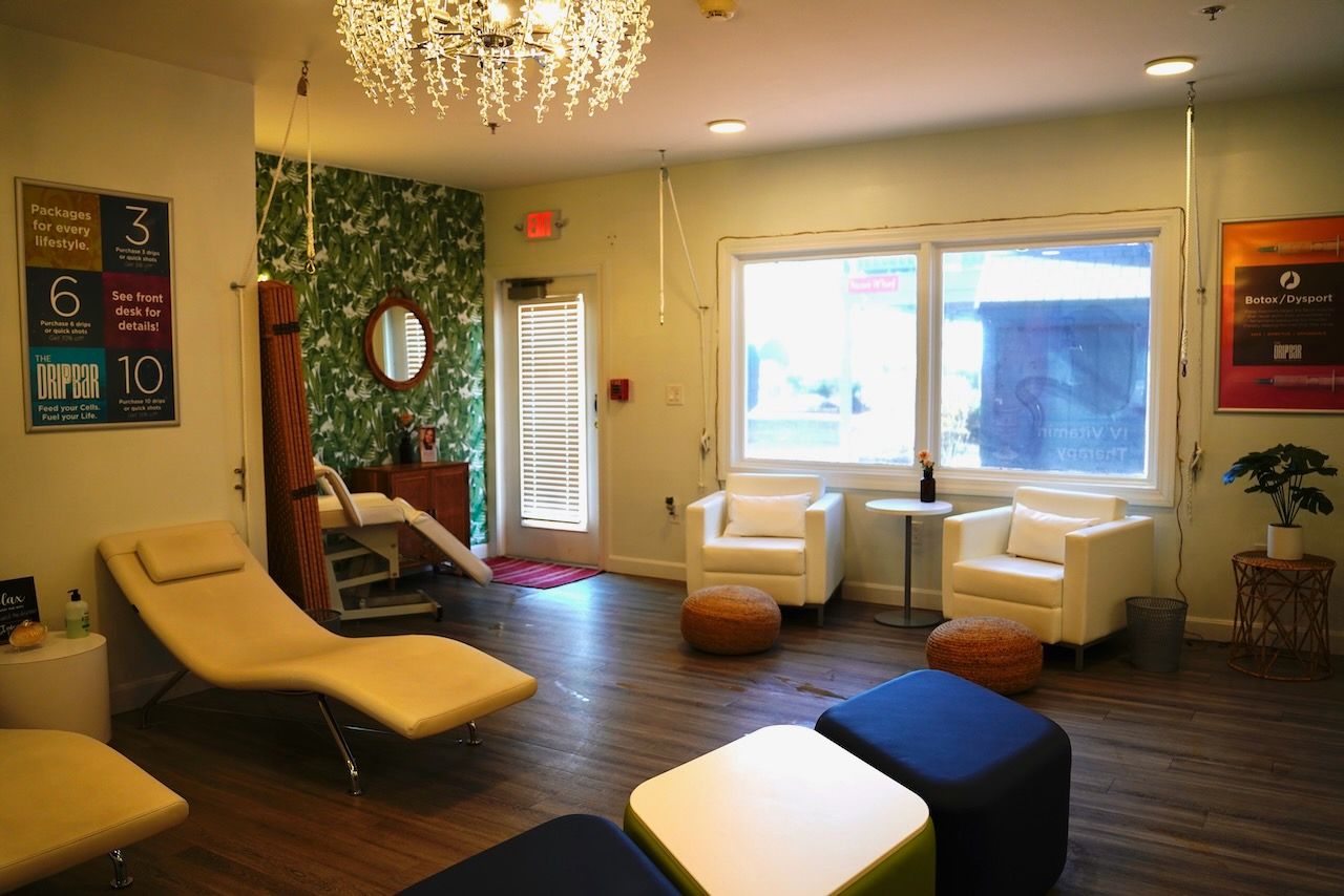 A living room with chairs , ottomans and a chandelier.