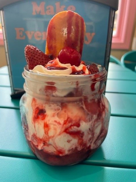 A jar of ice cream with strawberries and whipped cream on a table