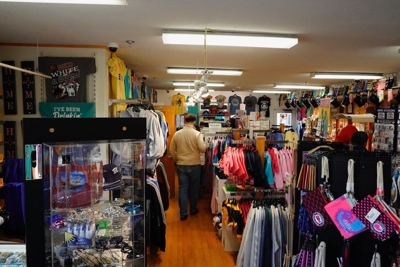 A man is walking through a clothing store filled with clothes.