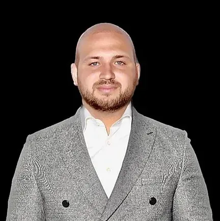 A bald man with a beard is wearing a grey suit and white shirt.