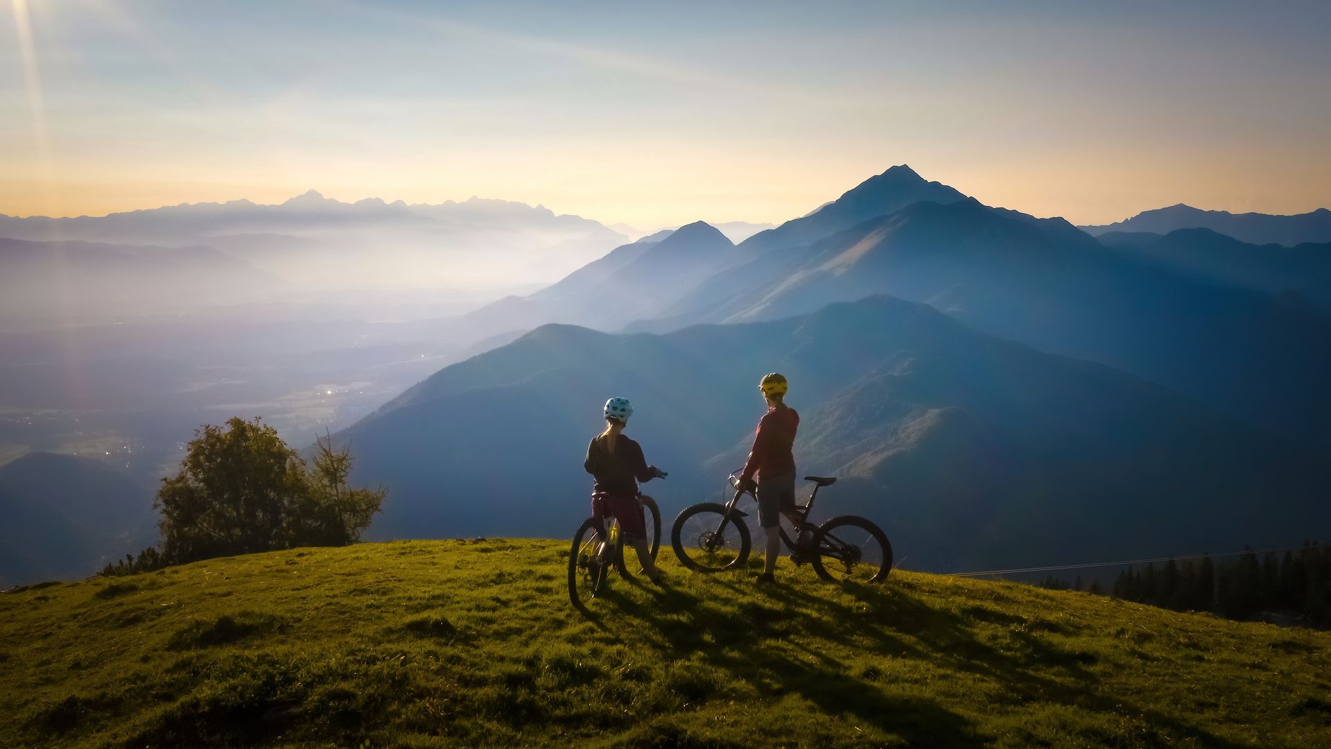 Two people are standing on top of a hill with bicycles.