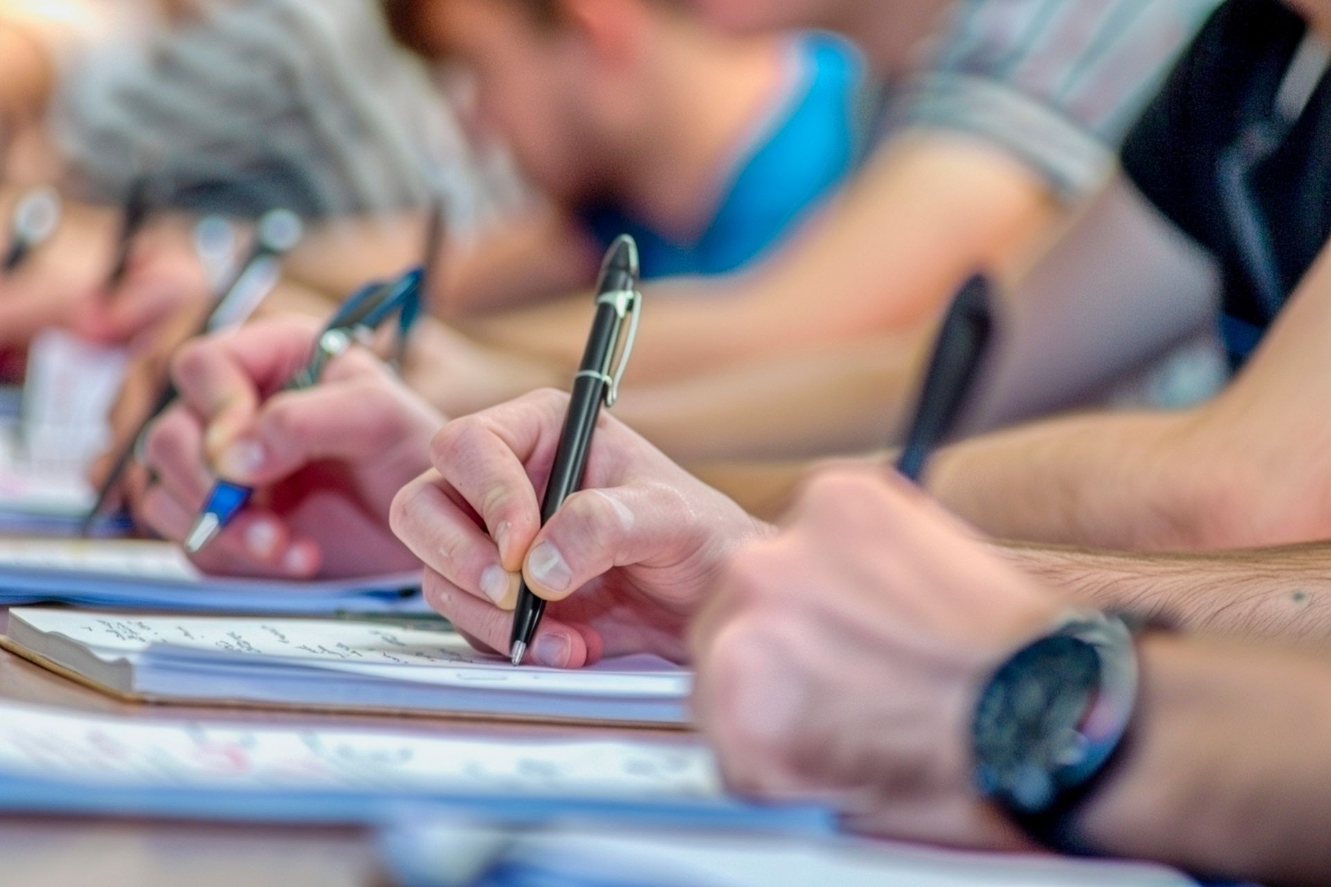 A group of people are sitting at a table writing in notebooks.