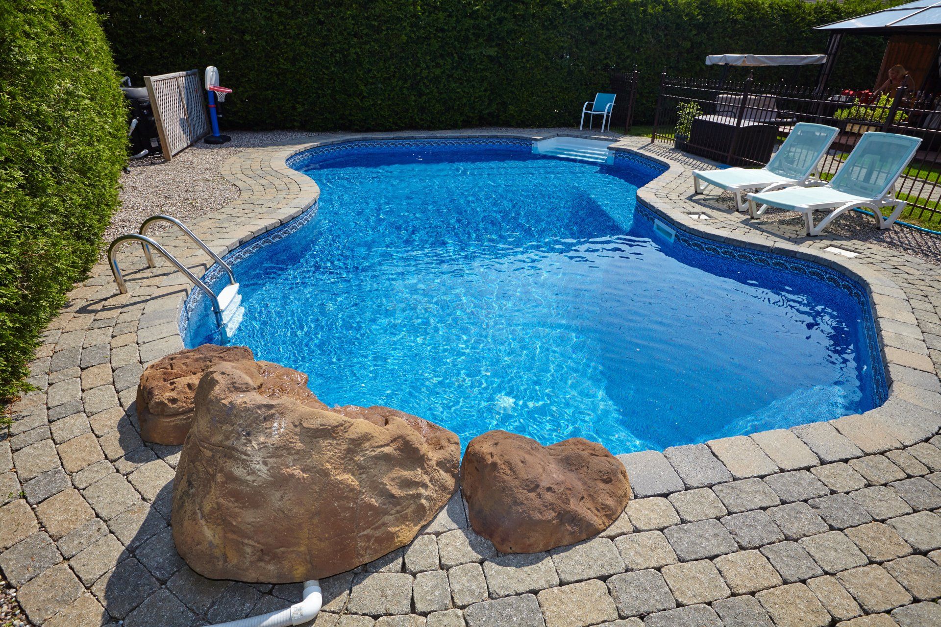 a in ground pool with grey brick flooring with pool furniture around it