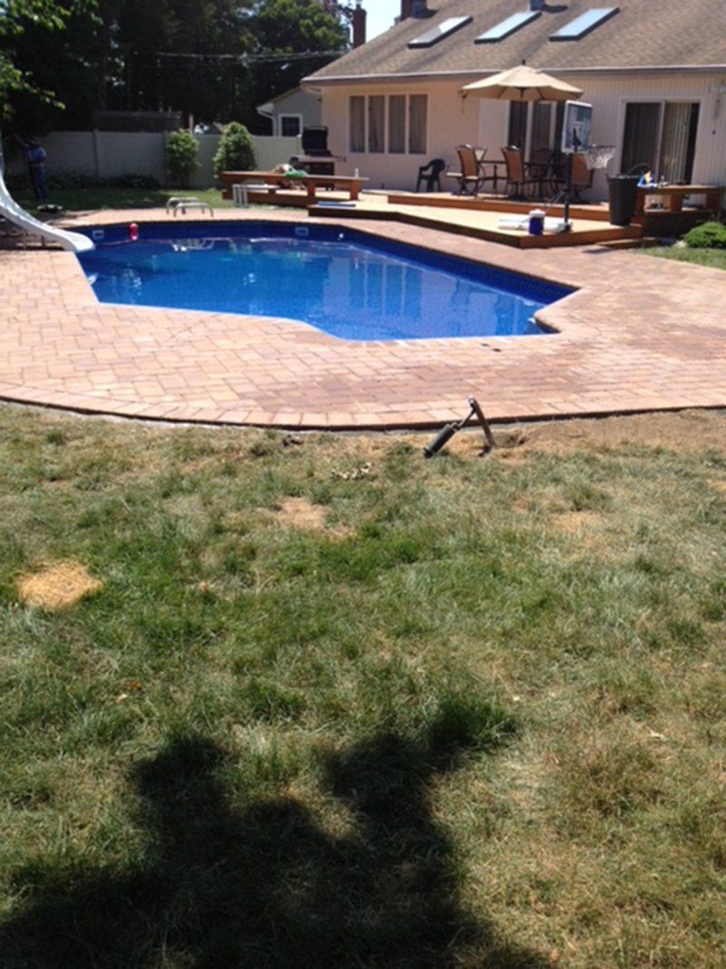 A in ground pool with a white slide attached, red bricks for patio around pool
