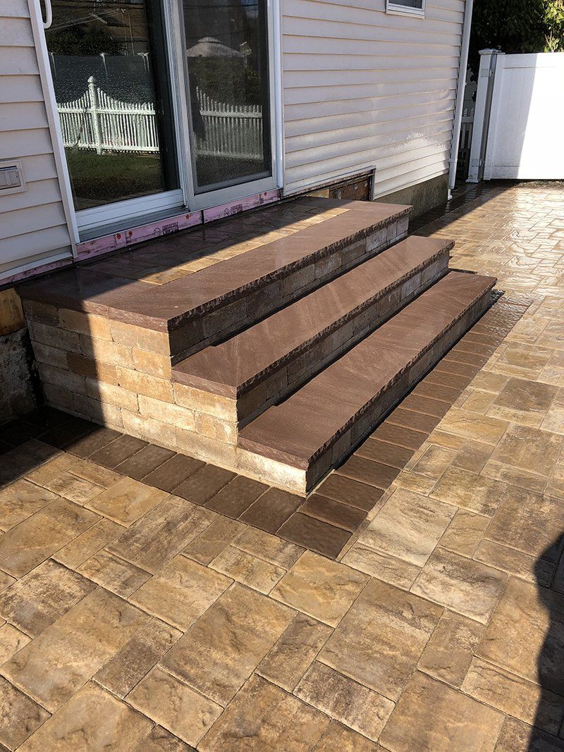 multi step stoop made of dark brown stone leading to a stone patio