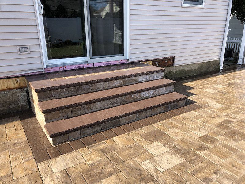 multi step stoop made of dark brown stone leading to a stone patio