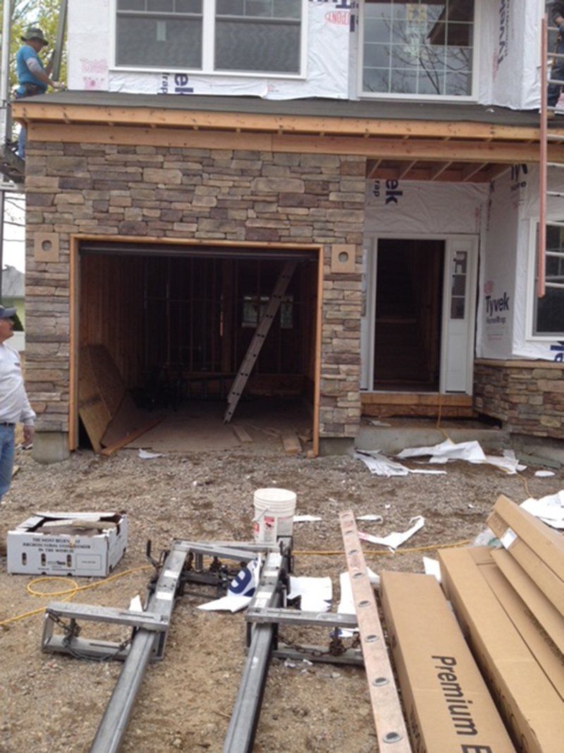 new constructed home with stone work around garage door, men working around house