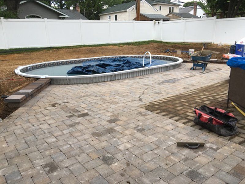 a covered in ground pool with a brown stone patio