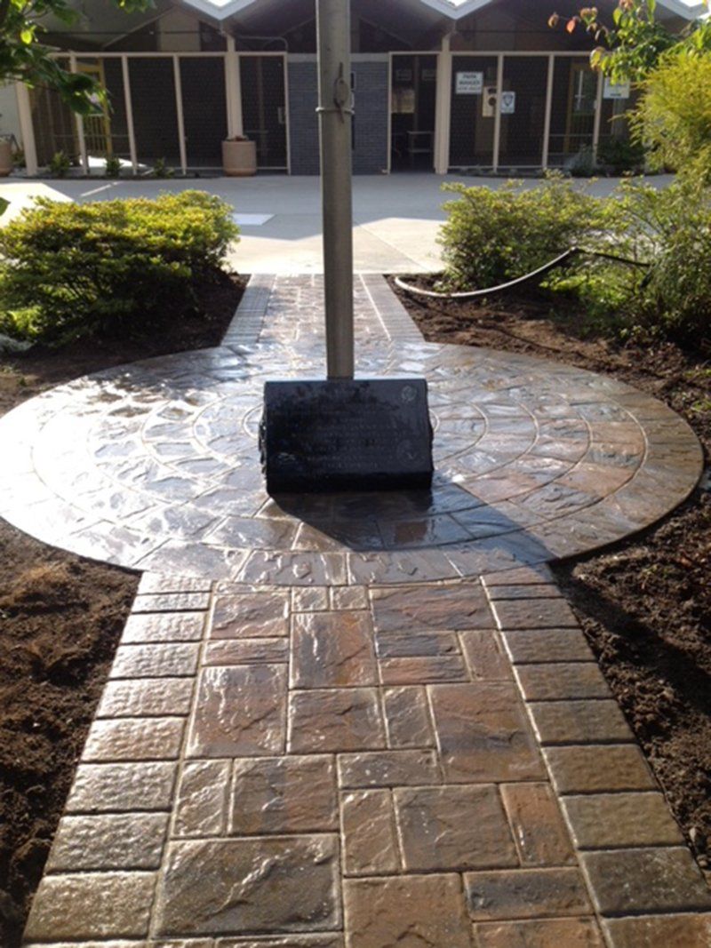 wet walkway made of stones that has a flag pole with a memorial stone at the base