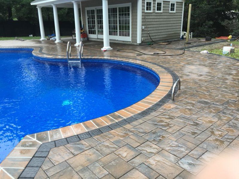 A in ground pool with grey bricks for patio, with a pool house next to it.