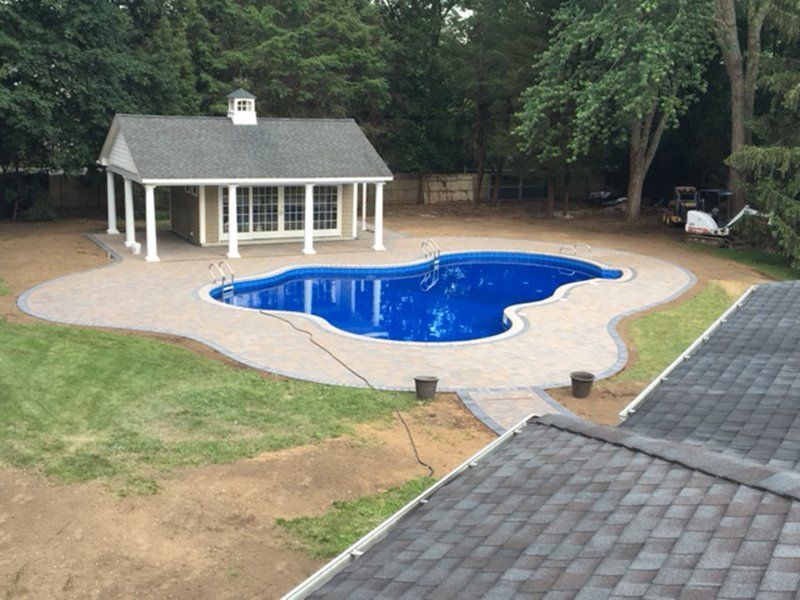 A in ground pool with grey bricks for patio, with a pool house next to it.