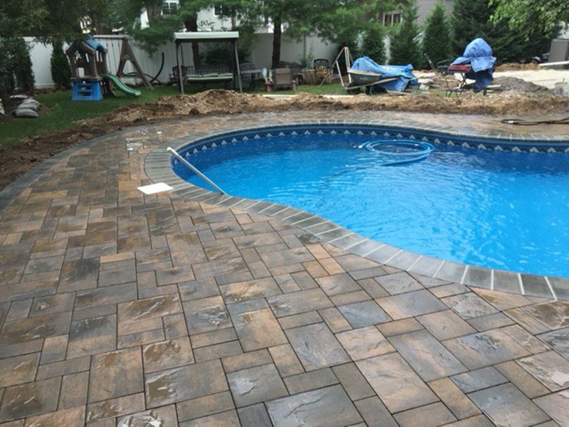 A in ground pool with grey bricks for patio with yard work being done