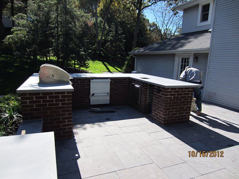 out door metal bbq grill surrounded by red brick counter with a light grey slab top