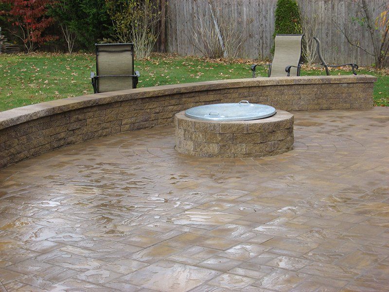 round brown stone fire place with a brown stone patio with a stone wall fence