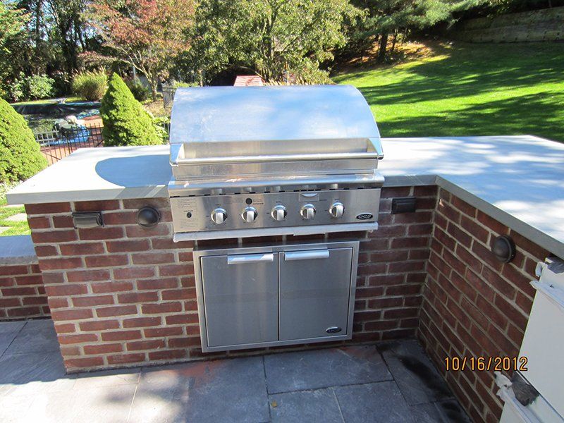 out door metal bbq grill surrounded by red brick counter with a light grey slab top