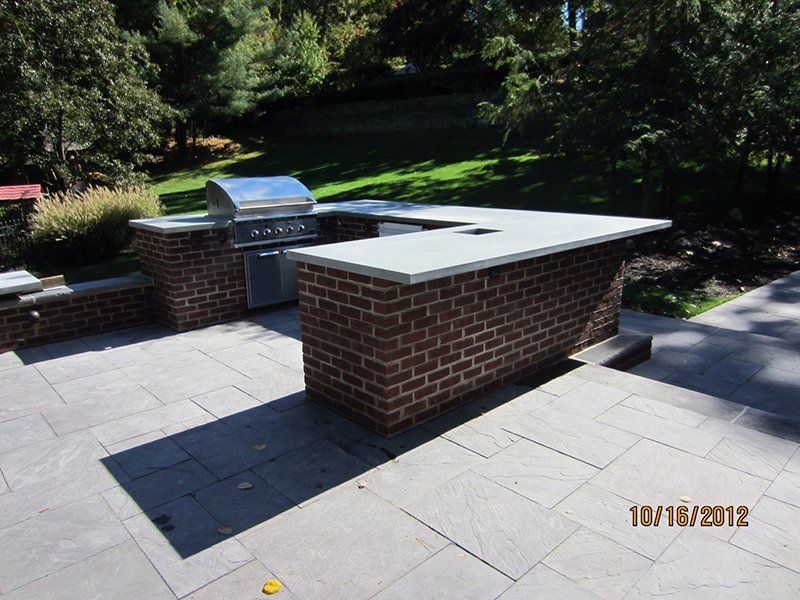 out door metal bbq grill surrounded by red brick counter with a light grey slab top