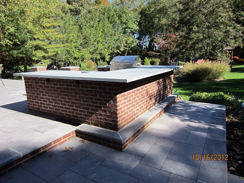 out door metal bbq grill surrounded by red brick counter with a light grey slab top