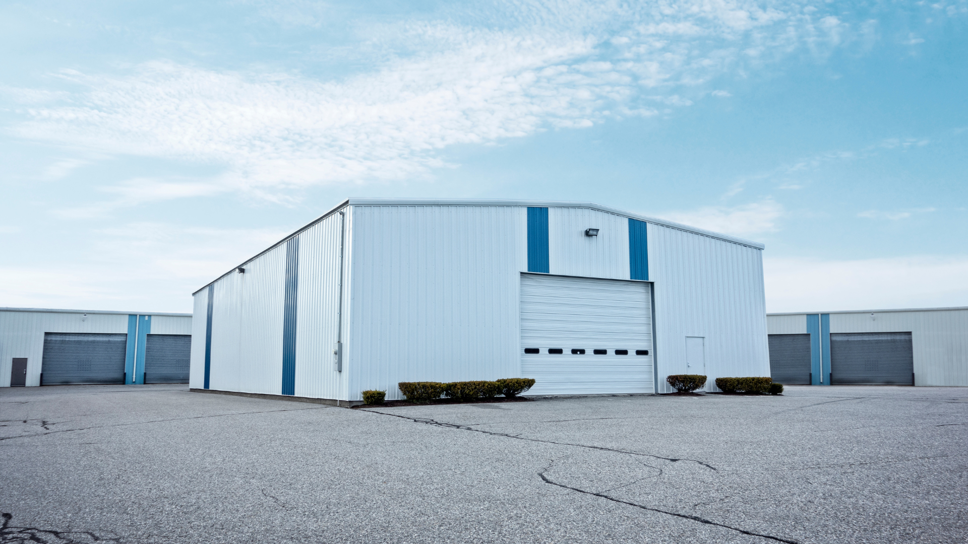 White industrial building with blue trim under a cloudy sky.