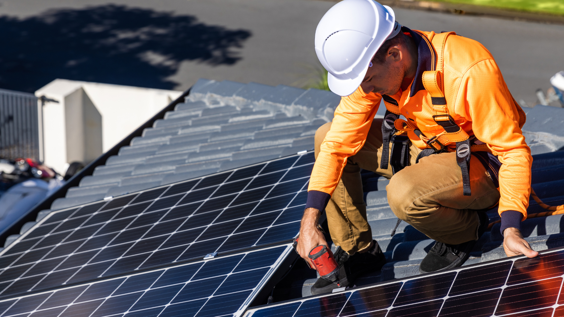 Solar panel installer, wearing safety gear, working on a rooftop.