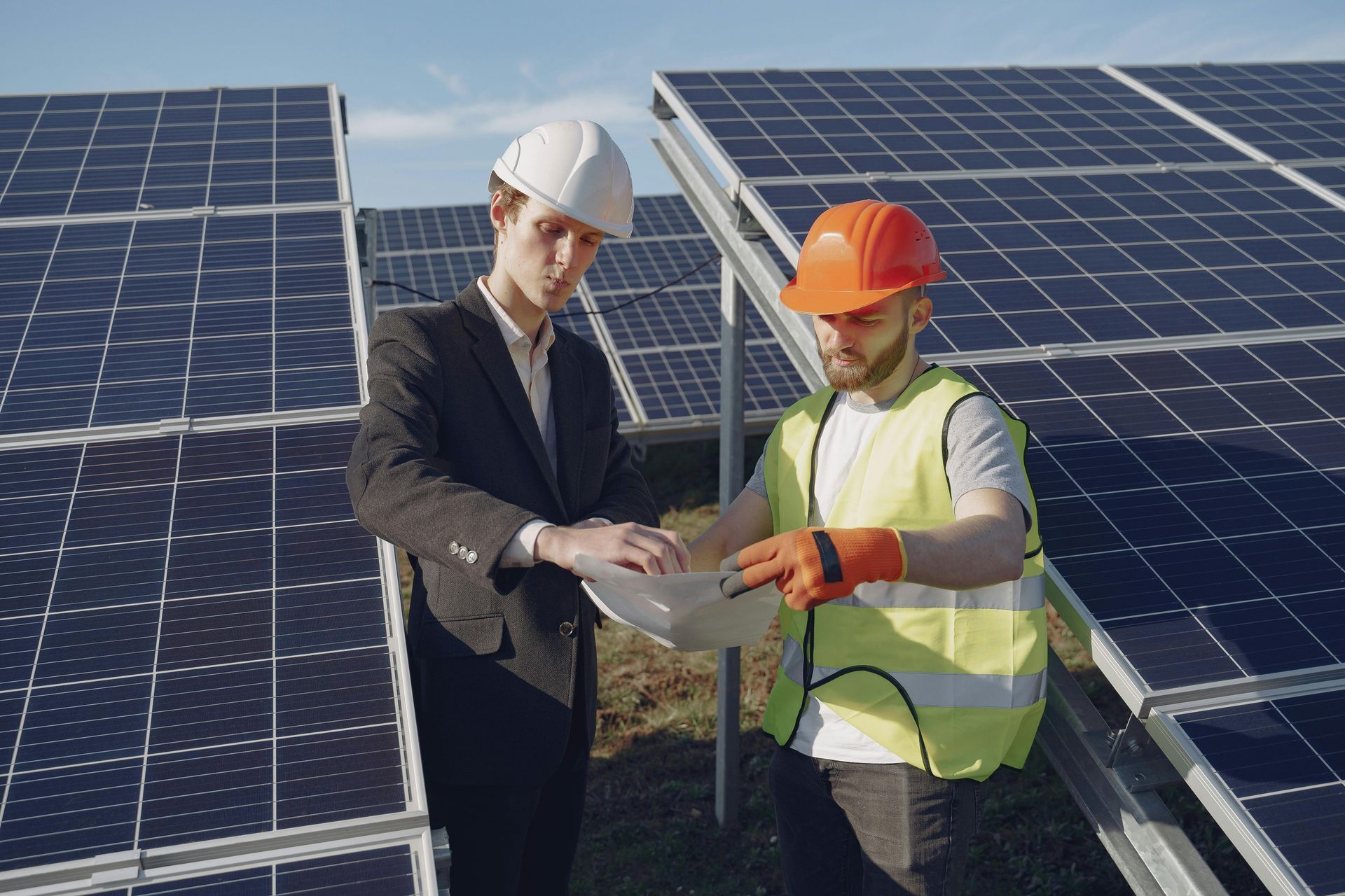 Two workers in hard hats reviewing plans at a solar panel site