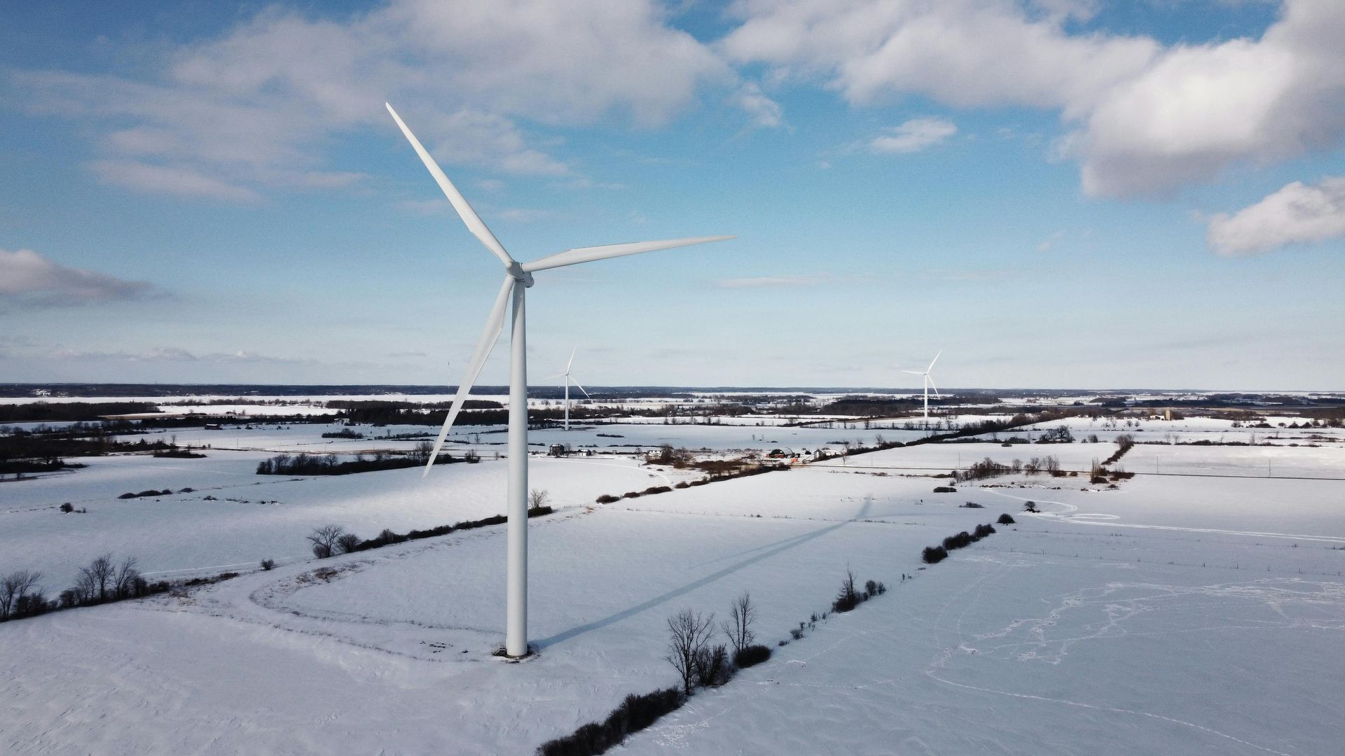 Snow-covered wind turbine in a winter field under a cloudy sky