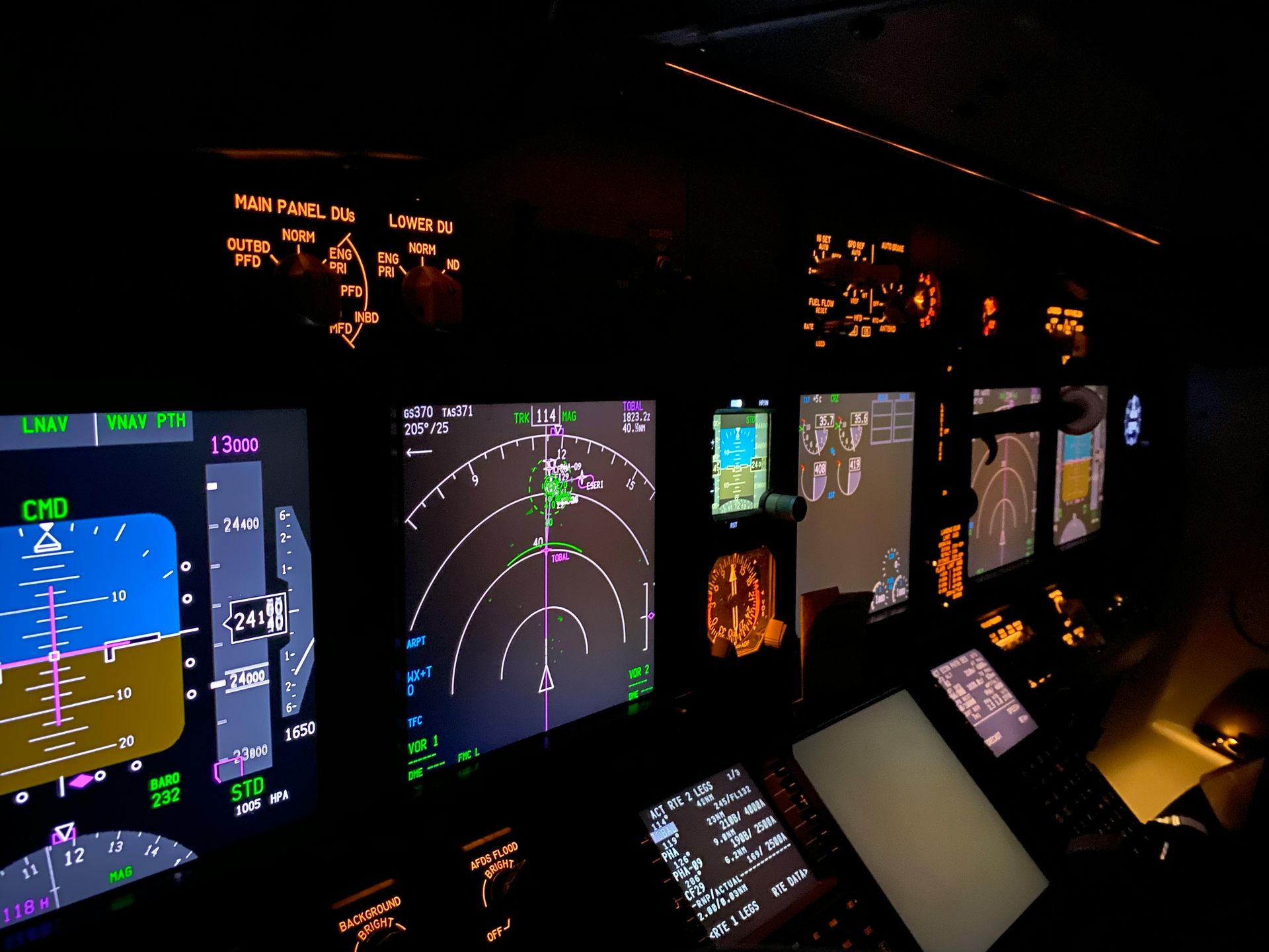Illuminated cockpit displays during a nighttime flight. Various instruments show data with green, yellow, and orange colors.