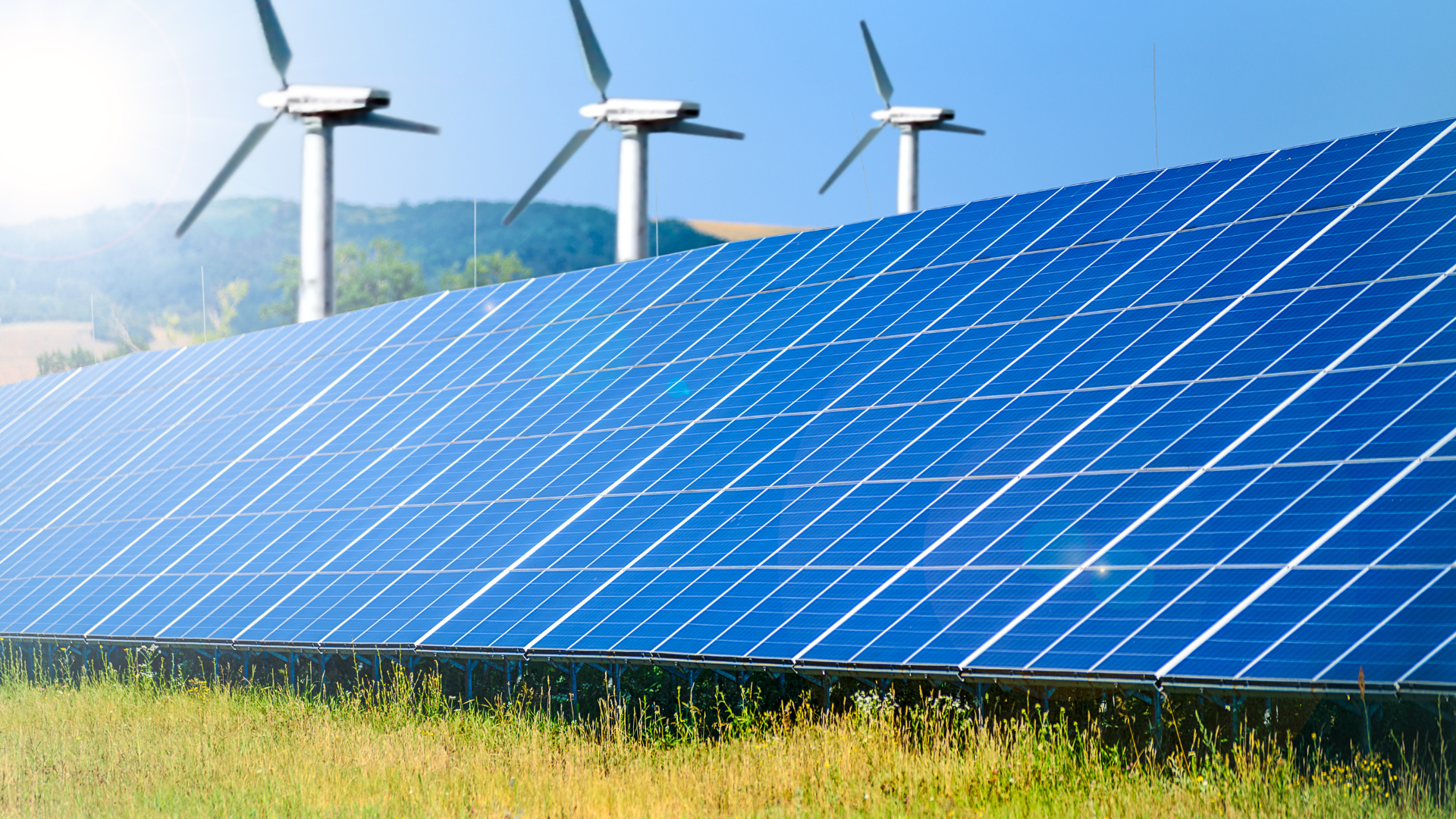 Solar panels in field with wind turbines in background, generating renewable energy.