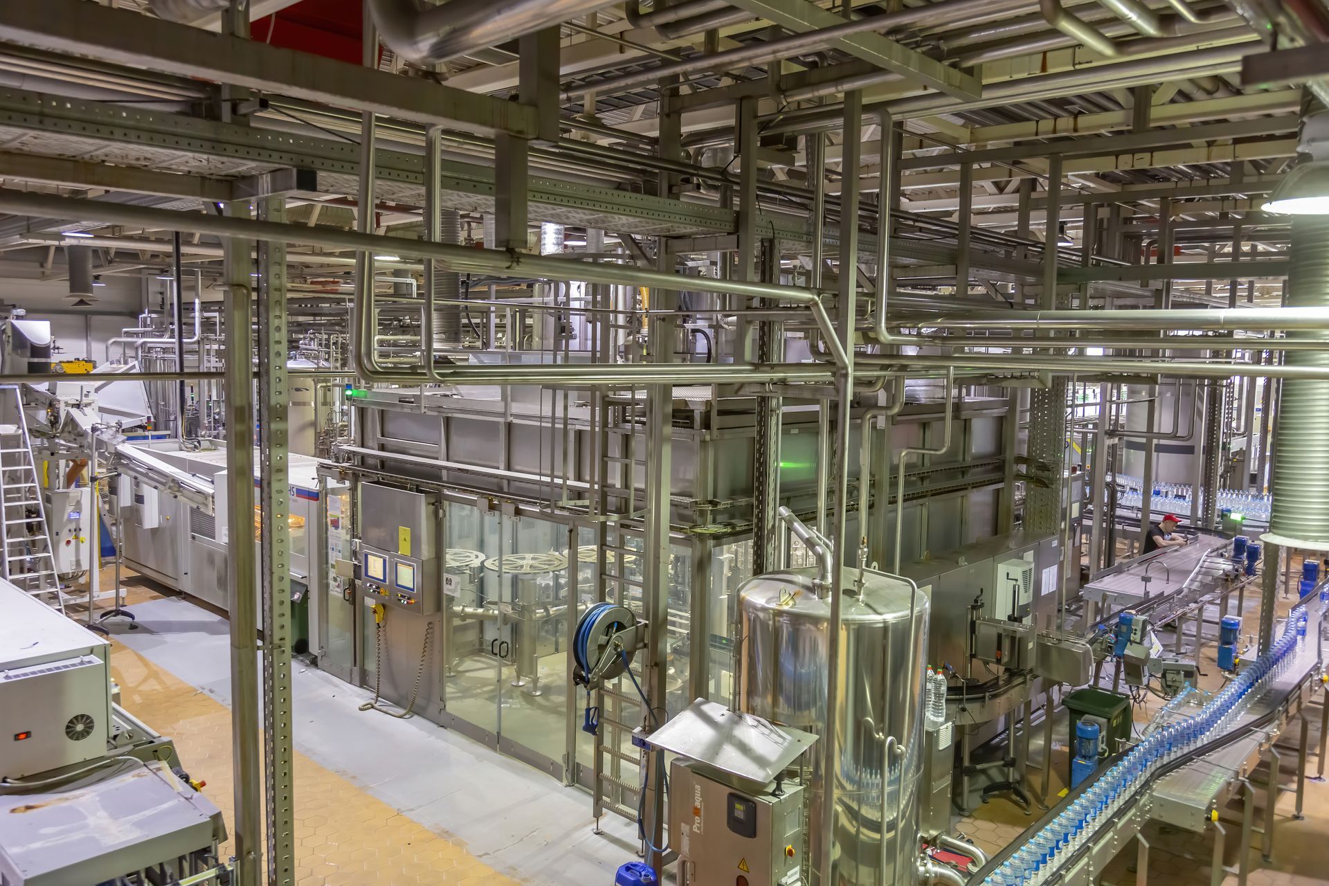 Factory interior with stainless steel pipes, machinery, and production lines.