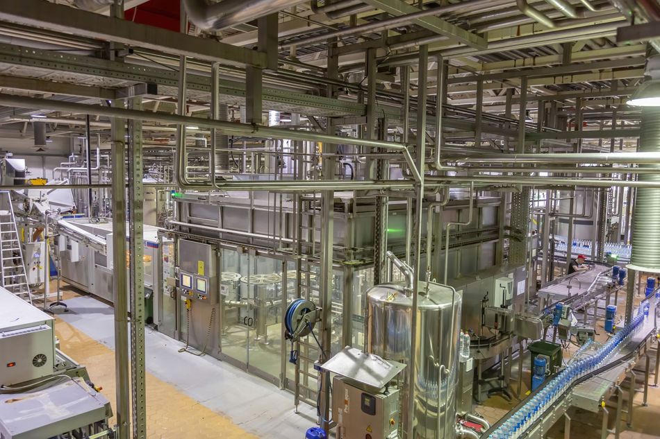 Industrial interior of a factory with stainless steel pipes, machinery, and conveyor belts.