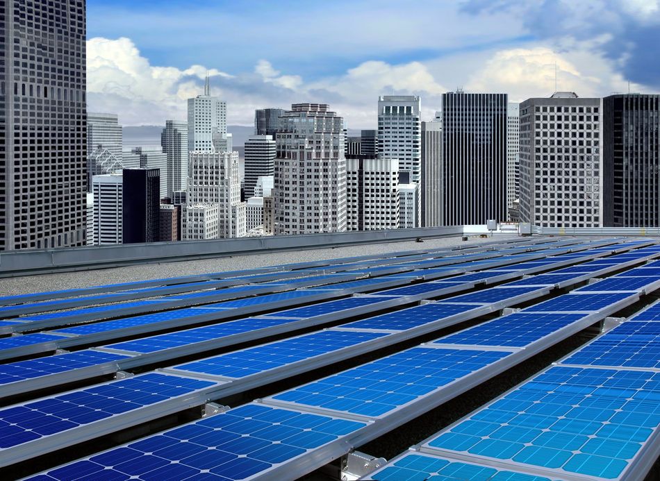 Rooftop solar panels in front of a city skyline with blue sky and clouds.