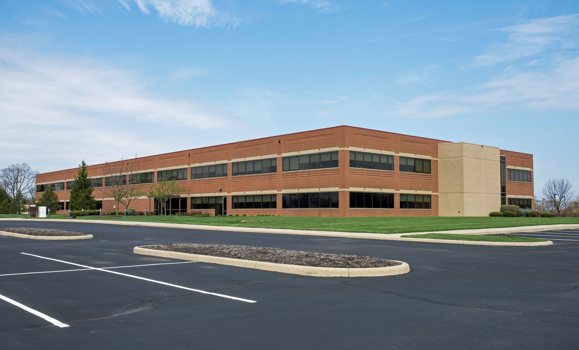 Two-story brick office building with dark-tinted windows, viewed from a parking lot under a blue sky. Two-story brick office building with dark-tinted windows, viewed from a parking lot under a blue sky.