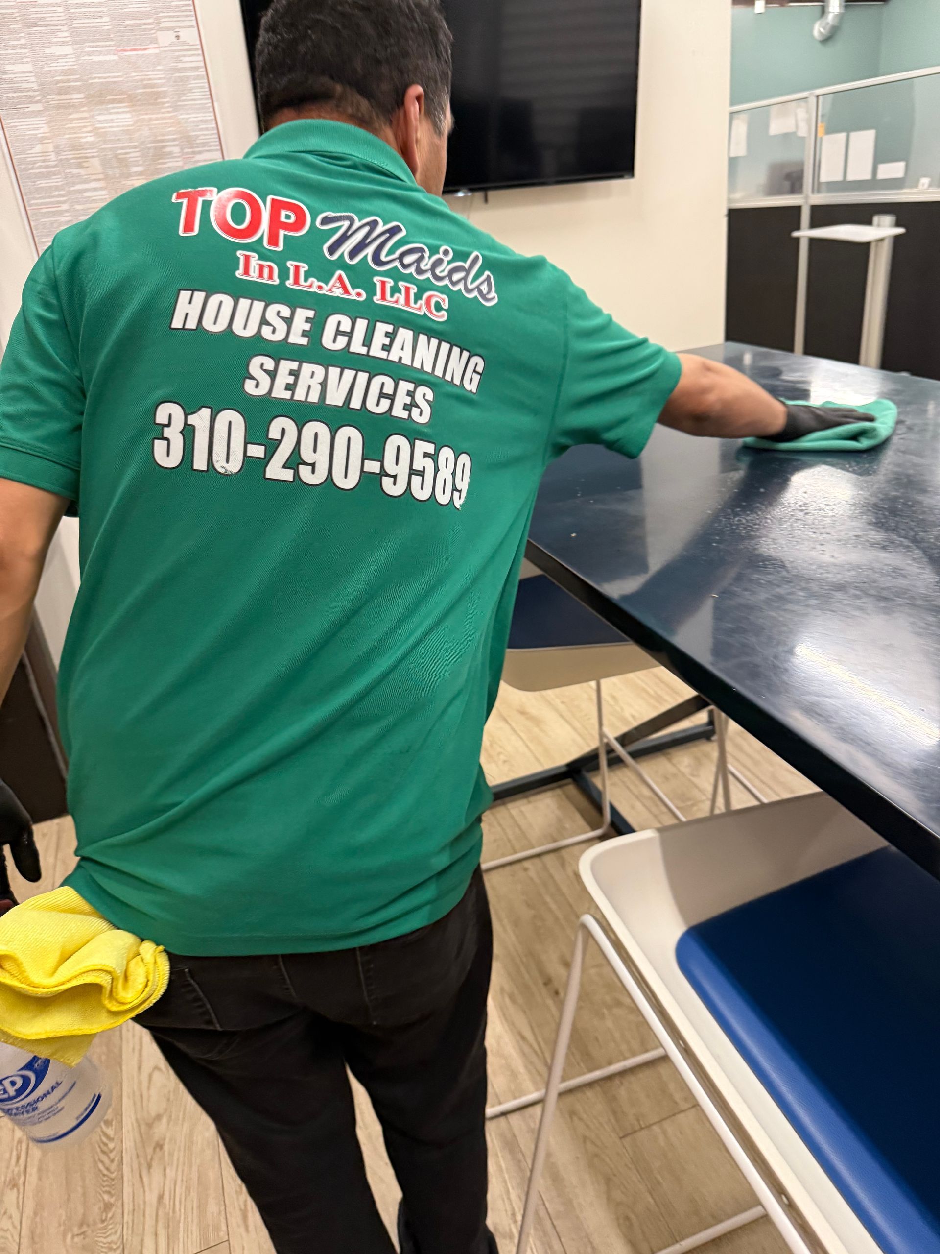 Person in green shirt with company logo cleans a blue table with a cloth.