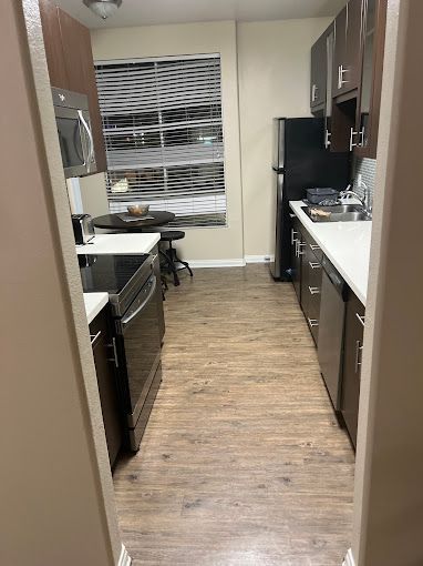 A kitchen with wooden floors , stainless steel appliances , a refrigerator , and a table.