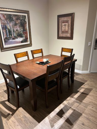 A dining room with a wooden table and chairs and a painting on the wall.
