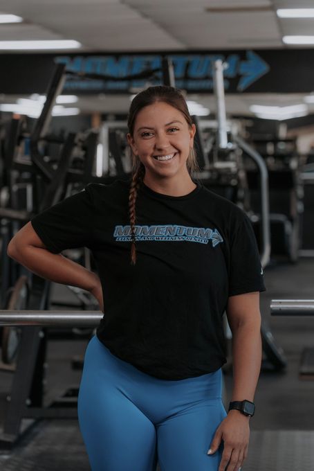 A woman in a black shirt and blue pants is standing in a gym.