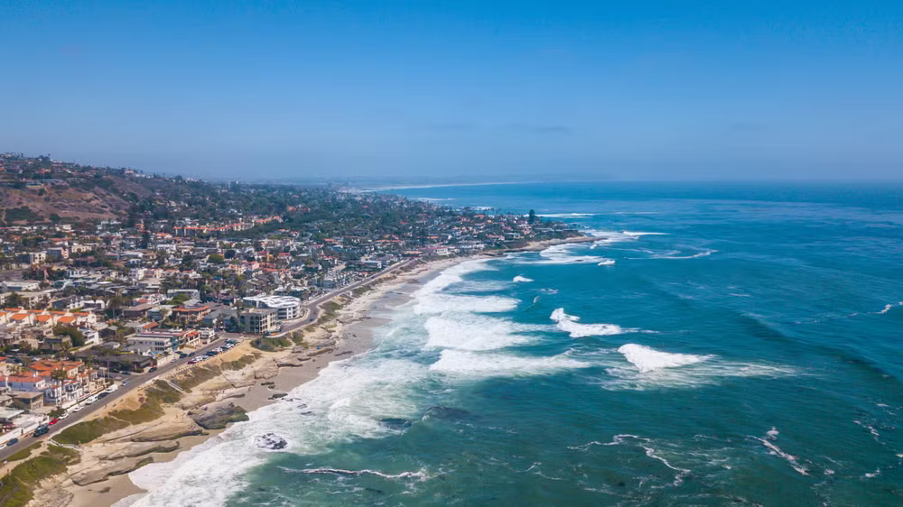 an aerial view of a beach with waves crashing on the shore and a city in the background .