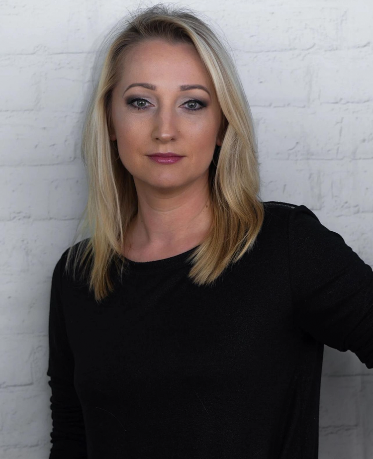 A woman in a black shirt is standing in front of a white brick wall.
