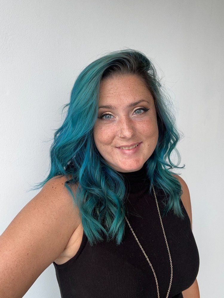 A woman with blue hair is wearing a black tank top and a necklace.