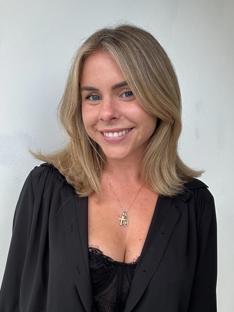 A woman wearing a black jacket and a necklace is smiling for the camera.