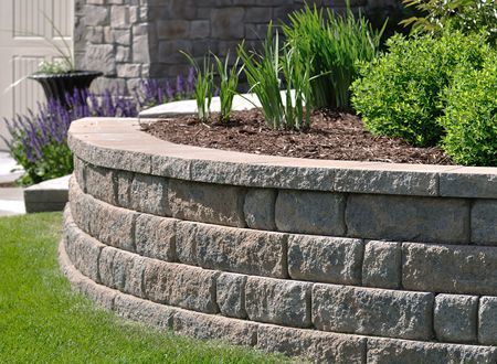 A stone wall with plants growing on it in front of a house.