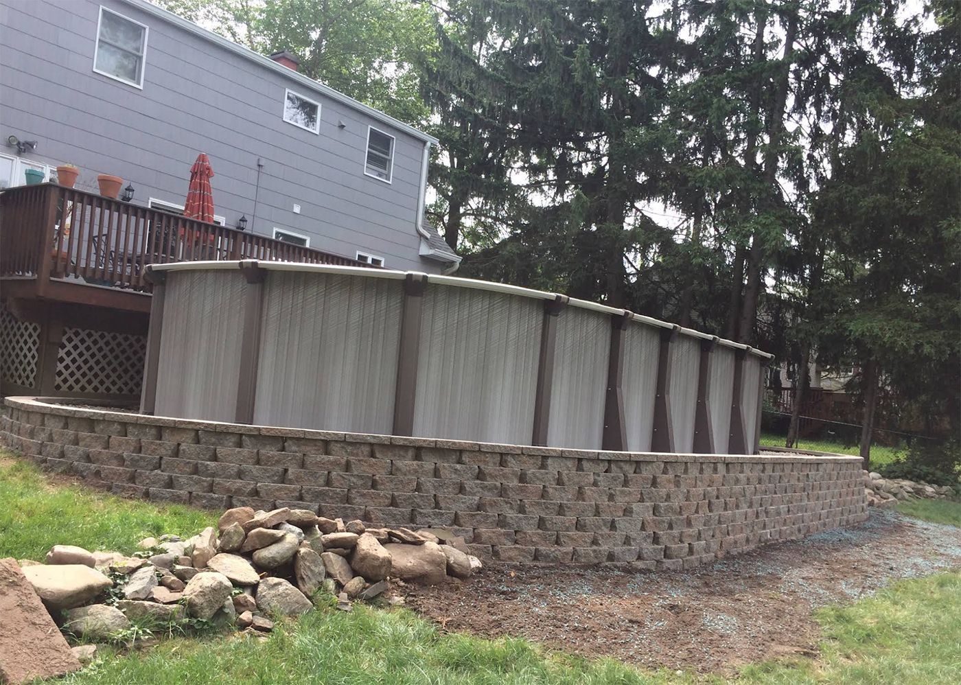 A large swimming pool is sitting on top of a brick wall in front of a house.
