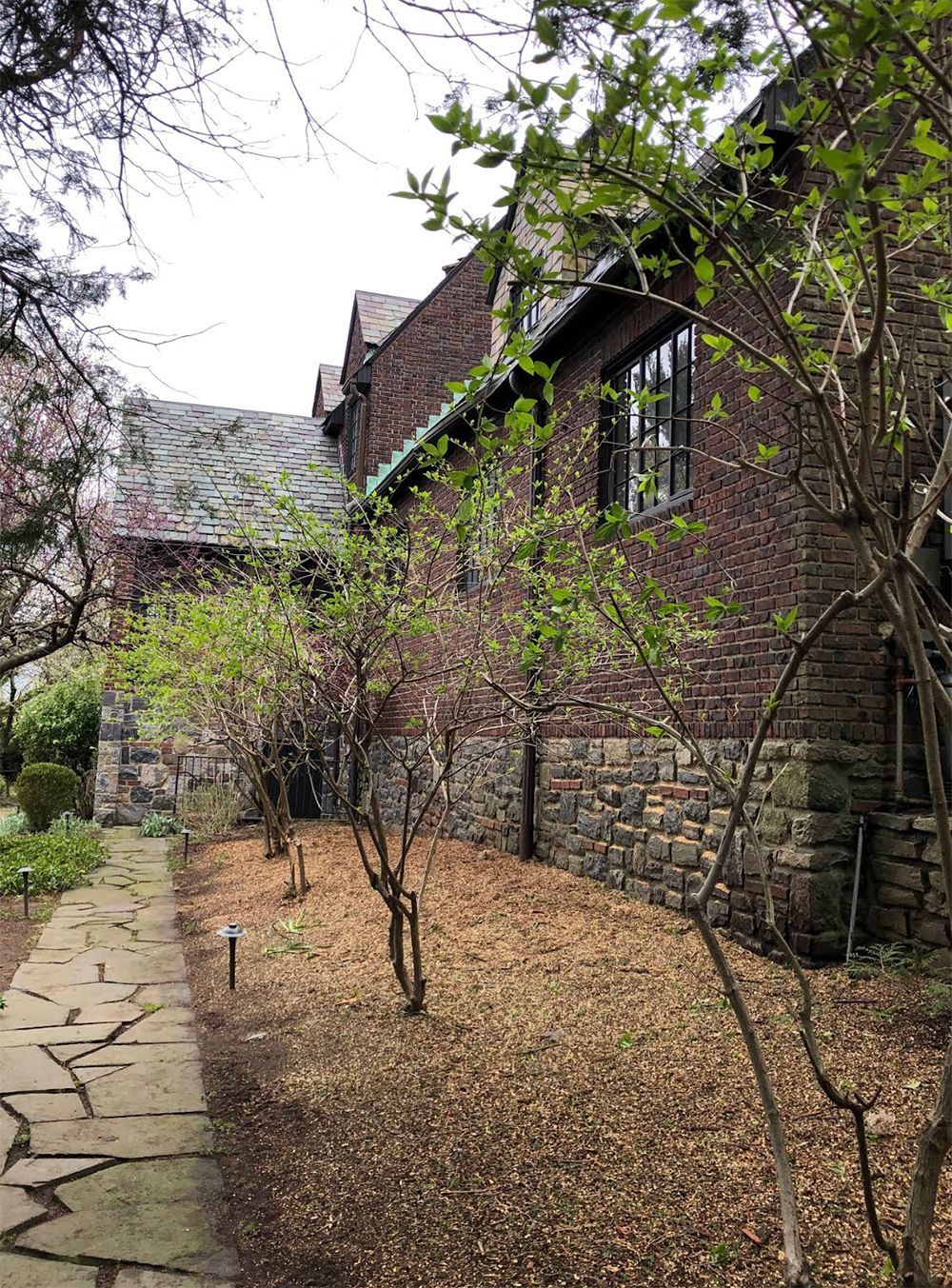 A stone walkway leading to a brick building with trees in front of it.