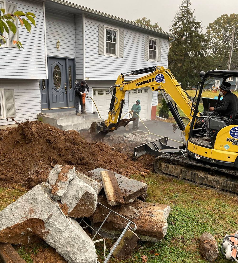 A yellow excavator is digging a hole in front of a house.