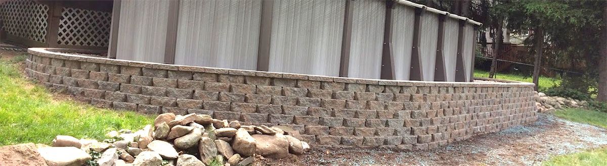 A stone wall is surrounding a shed in a yard.