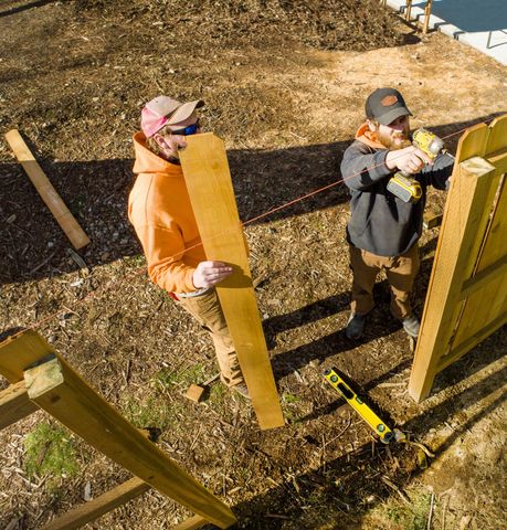 Two men are working on a wooden fence near a body of water