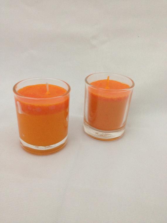 Two orange candles in shot glasses on a white surface.