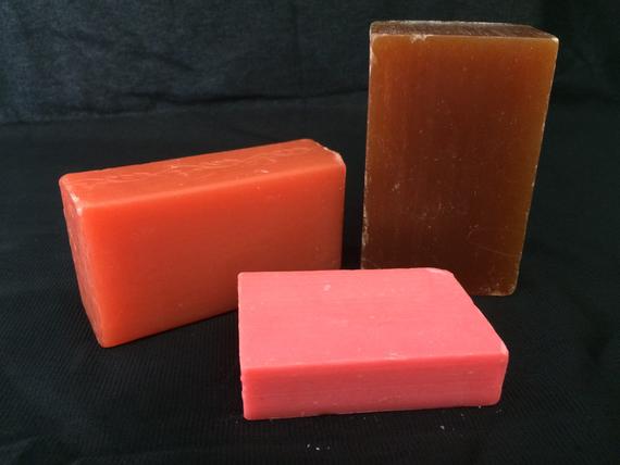 Three different colored bars of soap on a black surface