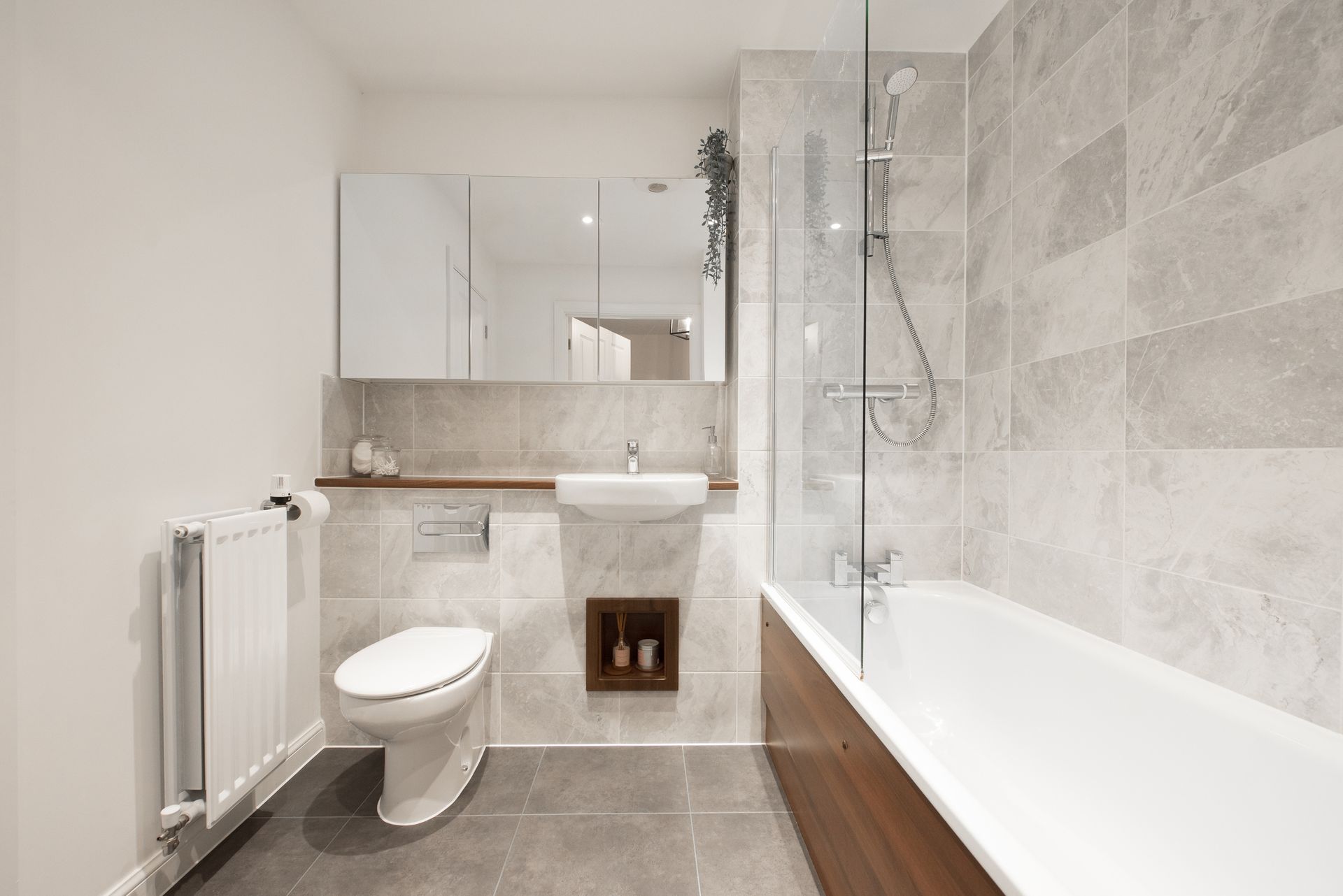 Modern bathroom with gray tiled walls, white toilet, and a bathtub.